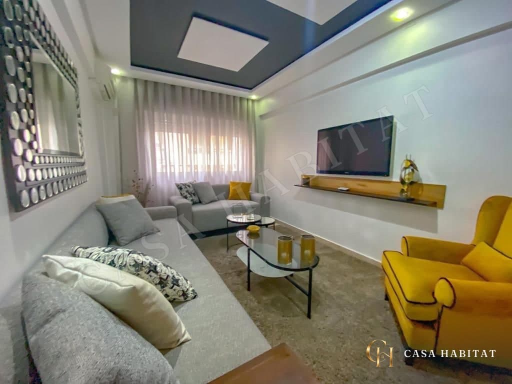 Salon avec canapé gris, fauteuil jaune et téléviseur mural